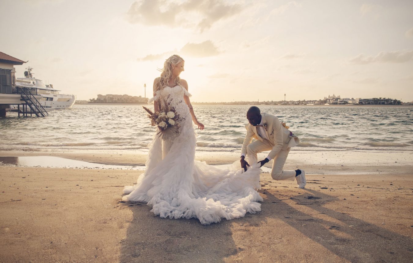 A groom adjusting his bride dress train at the beach